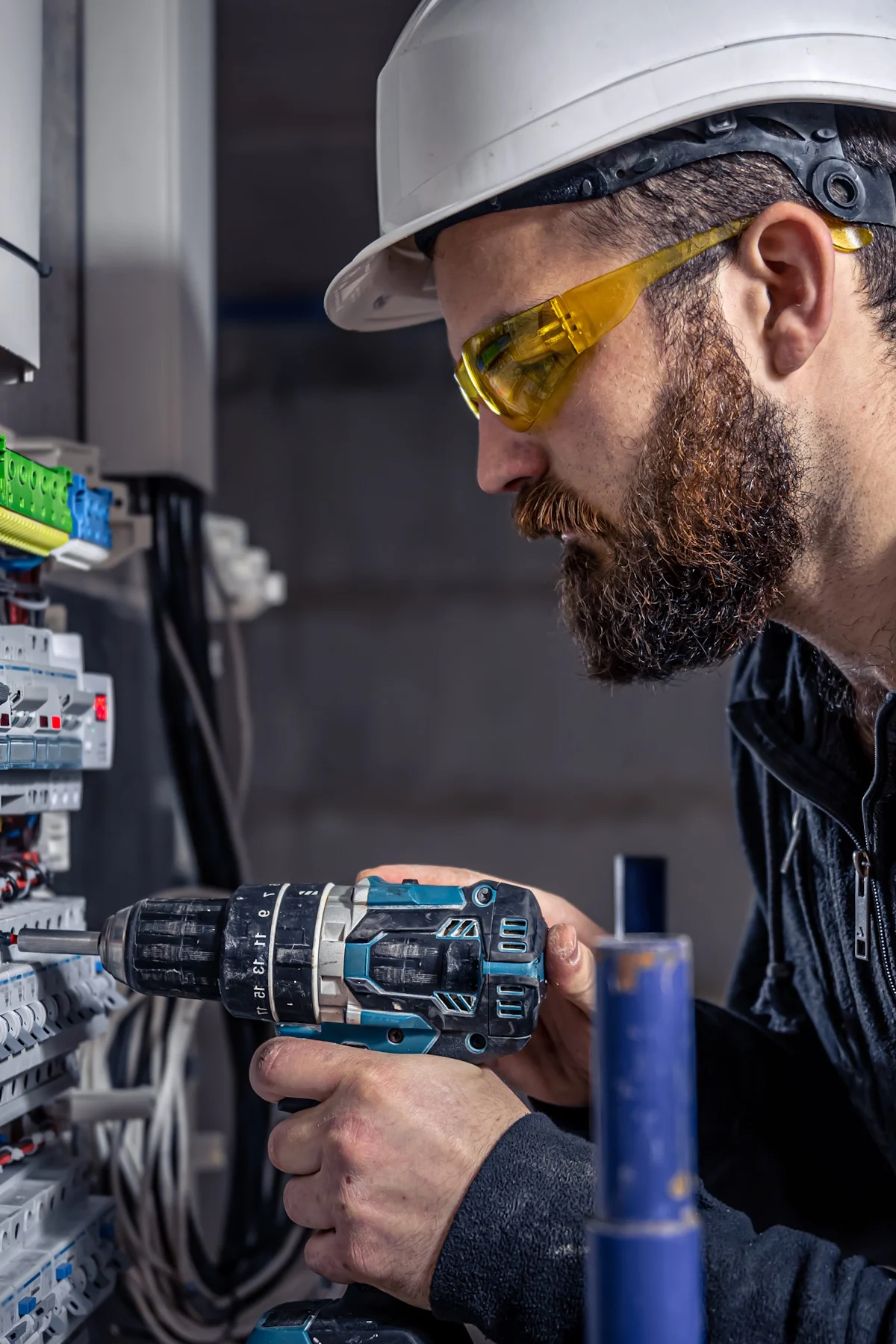 A male electrician works in a switchboard with an electrical connecting cable.
